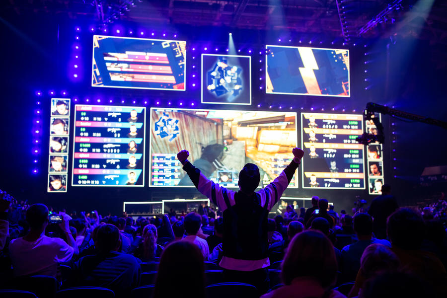 Big esports event. Video games fan on a tribune at tournament`s arena with hands raised. Cheering for his favorite team.  Photo 160802904 © Roman Kosolapov | Dreamstime.com